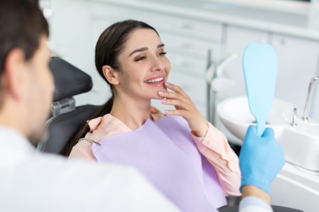 Smiling,Woman,Looking,In,Mirror,After,Dental,Procedure,In,Clinic, restorative dentist taylorsville