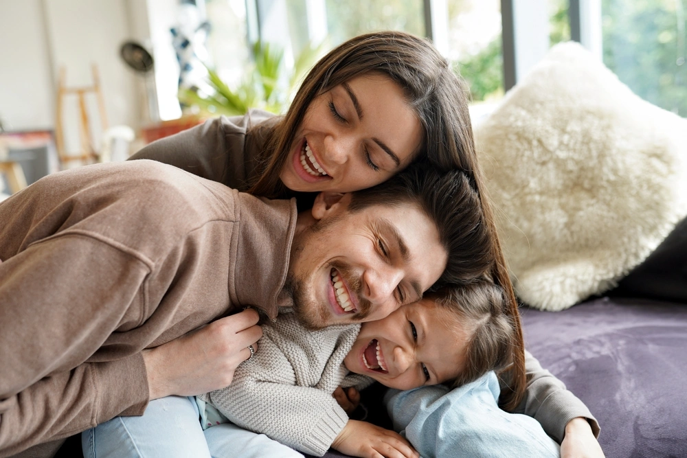 Laughing family of three cuddling on a sofa, promoting regular dental cleanings