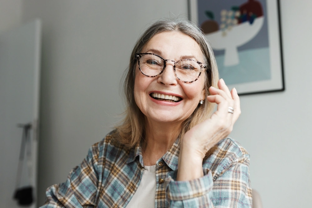 Smiling senior woman in glasses and a plaid shirt, illustrating comfortable dentures