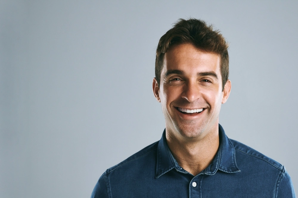Smiling man in a denim shirt showing even white teeth, illustrating dental veneers